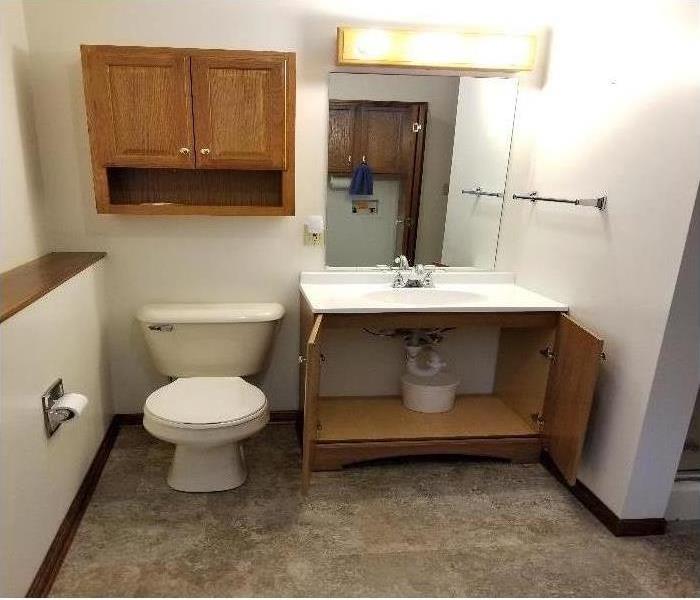 A bathroom with the cabinets under the sink open revealing underneath the sink