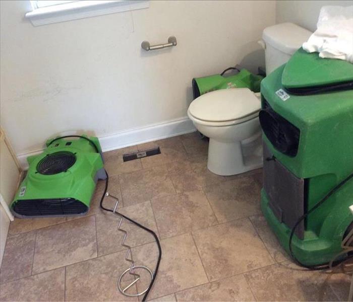 White toilet next to three green air movers.