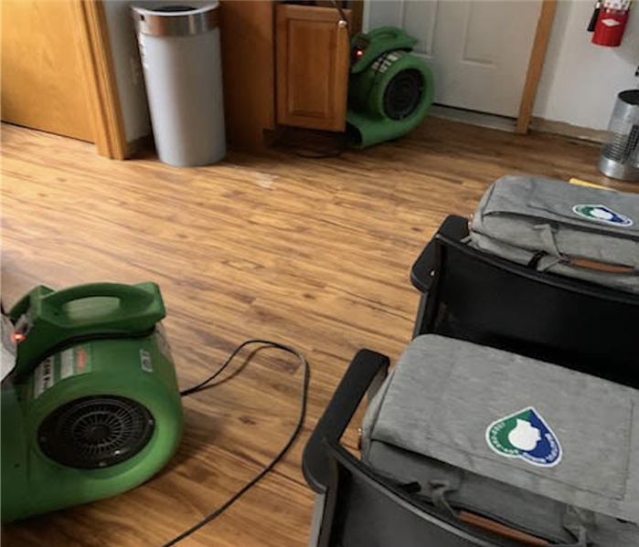 Room with wood flooring and two green air movers on the ground.